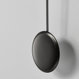 Modern black oval pendant light hangs vertically from ceiling, emitting sleek minimalist design.