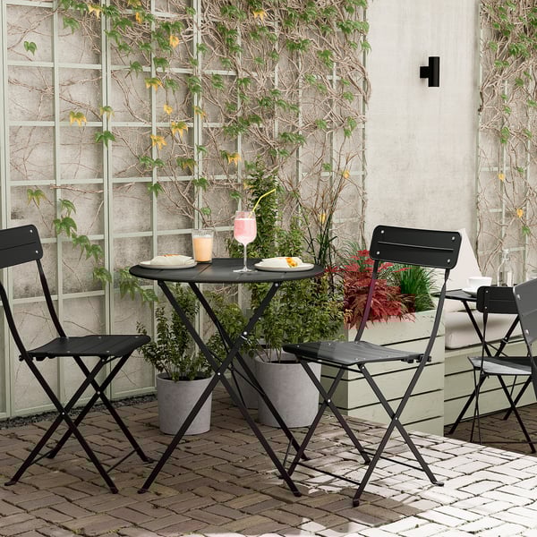 Black metal balcony set with foldable table and chairs, potted plants.