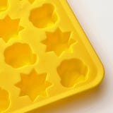 Bright yellow ice tray with star-shaped molds on white surface.