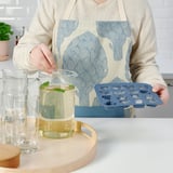 Person places ice cubes from SURSÖT tray into drink pitcher, enhancing summer feel with playful ice shapes.
