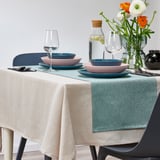A table set with colorful plates, glasses, and a green-blue runner on a white tablecloth.