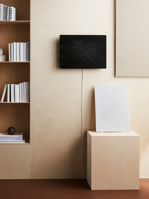 Black wifi speaker with picture frame on wall, white speaker on wooden stand, bookshelf below.