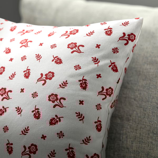 White cushion with red floral patterns, laid on a grey texture.