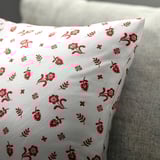 White cushion with red floral patterns, laid on a grey texture.