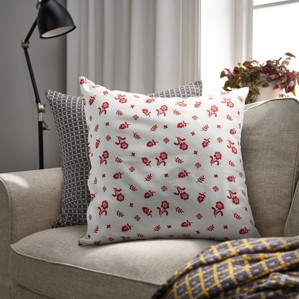 Grey floral cushion on beige sofa with other pillows, lamp, plant.