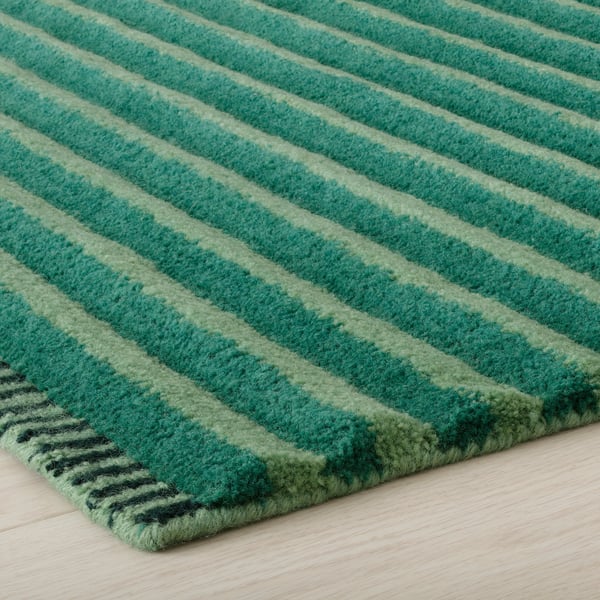 Striped wool rug with varied shades of green, texture detailed, laid on wooden floor.
