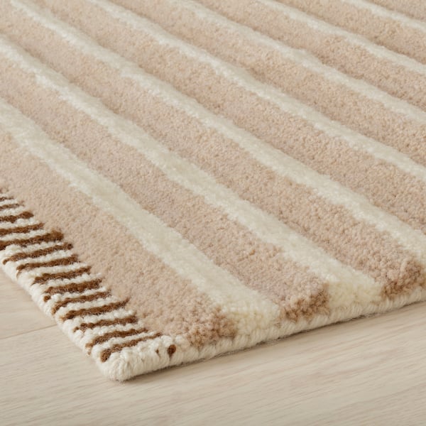Close-up of a textured, beige area rug with white stripes, showcasing its high-quality, hand-tufted wool design.