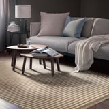 Modern living room with grey sofa, grey rug, nesting tables, lamp, and books.