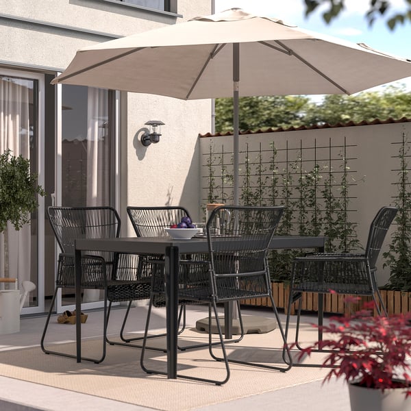 Patio seating with TALLSKÄR black chairs, beige umbrella. Rattan design, under large umbrella, surrounded by plants.