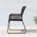 Black outdoor chair with woven rattan, designed for comfort and durability, positioned against a light wall with a plant.