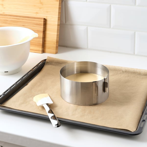 Metal baking ring on parchment-lined tray, with brush and bowl, preparing cake batter.