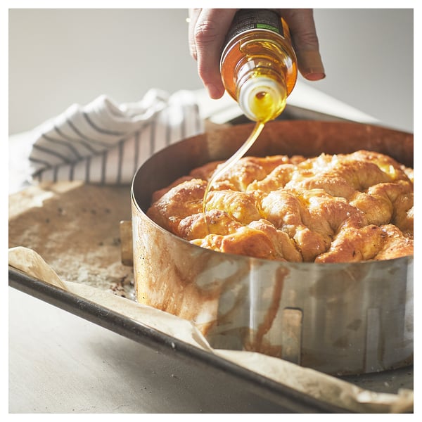 Person drizzling honey on golden brown baked treat in round metal pan.