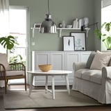 Modern living room with grey rug, light grey armchair, round white coffee table, wooden decor, and large window.
