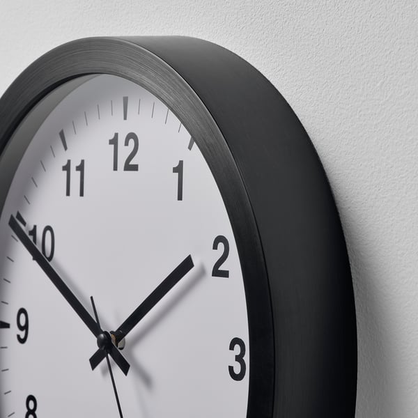 A round wall clock with a black frame and white face displaying black numbers and hands, showing the time as 10:10.