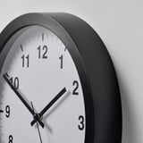 A round wall clock with a black frame and white face displaying black numbers and hands, showing the time as 10:10.