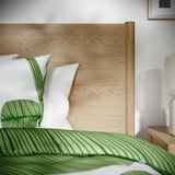 Modern bed with light wood headboard, white pillows, green accents, clean decor.