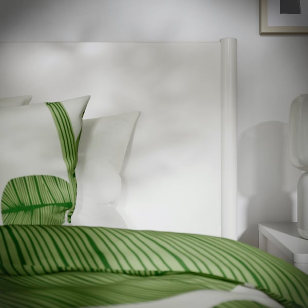 Neat bedroom with off-white TONSTAD bed, green striped bedding, and white walls. Soft-closing drawers under the bed.
