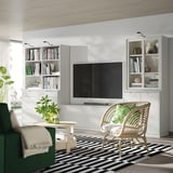Modern living room with white TONSTAD tv unit, shelves, and wicker chair. Flat screen tv, books, and plants enhance the minimalist decor.