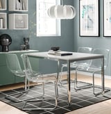 Modern dining set with acrylic chairs, white table, and pendant light on a gray rug. Decorated shelves and window in background.