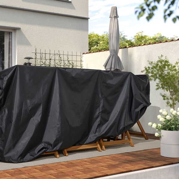 Outdoor dining set with dark, waterproof cover protecting against sun and rain. Plant and deck on right, white wall on left.