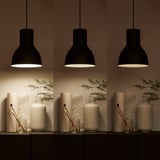 Three black pendants illuminate a shelf holding two striped vases, each with greenery, and small glasses with brushes.