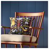 A bright orange chair with a colorful cushion. The cushion displays a swedish folk design in vibrant colors against a dark background.