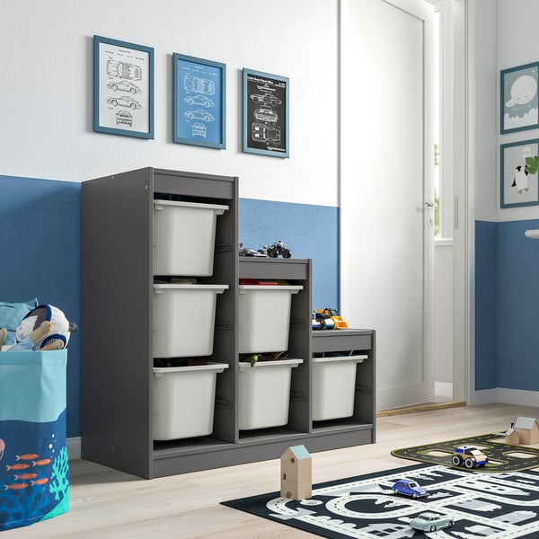 Childs room with TROFAST storage, bins, blue accents, charts. Toy basket, play mat, cars. Door to next room.