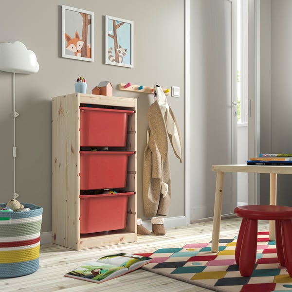 Kids room with TROFAST storage & red boxes. Near art, coats, and books table. Tall storage.