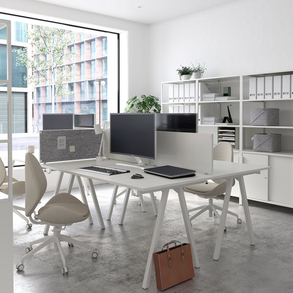 Modern white office setup with two desks, chairs, computers, and shelves against a large window.