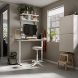 Home office with white TROTTEN desk, stool, shelves, and cabinets. Plants, laptop, and monitor on desk. Natural light from window.