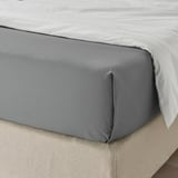 Close-up of neatly tucked gray bed sheet on a bed, showcasing its smooth, soft texture and precise fit.