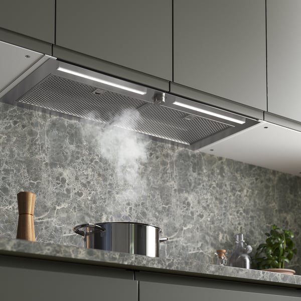 Modern kitchen with stainless hood emitting steam, integrated above marble backsplash, lighted and functional.