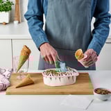 Person scooping ice cream onto cone with tools.