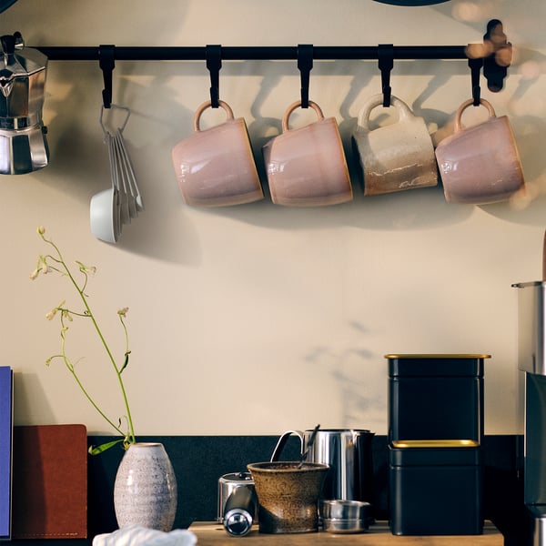 Kitchen counter with utensils. Mugs, a vase with flowers, and a ring of measuring cups hanging on hooks.