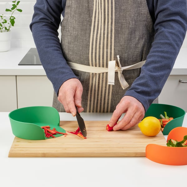 Person chops vegetables on a cutting board using UPPFYLLD bowl for easy prep and waste collection.