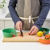 Person chops vegetables on a cutting board using UPPFYLLD bowl for easy prep and waste collection.