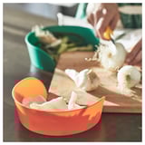 Bright orange UPPFYLLD bowl, filled with chopped white onions, sits on a counter. A person is seen preparing more onions on a chopping board nearby.