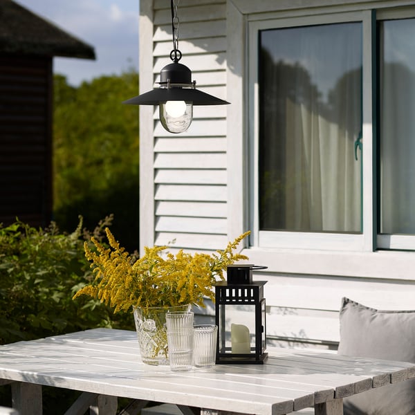 Black UPPLID lamp with glass shade, yellow flowers, outdoors. Classic, rustic design.