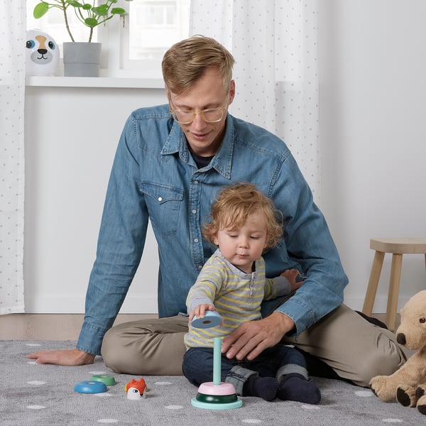 Adult and toddler playing with stacking toy on floor.