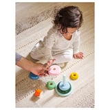 Child playing with UPPSTÅ stacking toy, pastel colors, on textured tan rug.