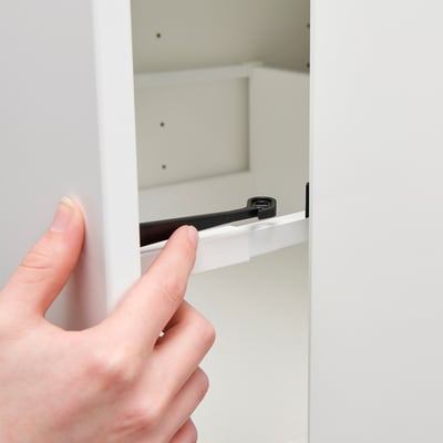Hand pressing UTRUSTA lock on kitchen cabinet.