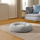 A cozy, round pet bed sits on a living room rug, designed for pets to curl up in, offering comfort and relaxation.