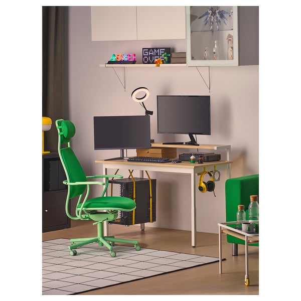 Modern green gaming desk setup with adjustable chair, monitors, keyboard, and headphones. Organized with shelves and cable management.