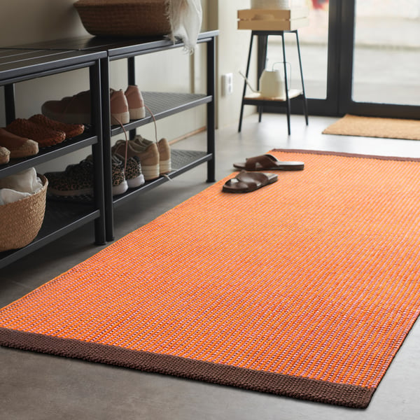 Bright orange VÄGOMRÅDE cotton rug with brown border, rectangular shape, grid design, fits under shoe rack, smaller than door mat.