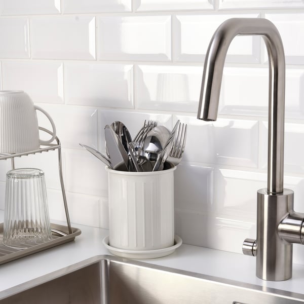 Stainless sink faucet with silverware in white holder on countertop.