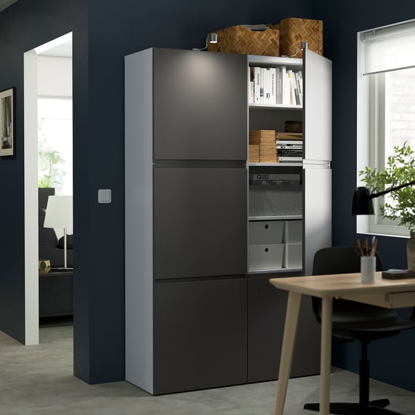 Modern office setup featuring grey storage units with integrated handles, holding books and files, adjacent to a wooden desk with a chair and lamp.