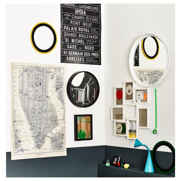 A wall decorated with a map, mirrors, and small picture frames. An abstract clock and various items are displayed on a ledge.