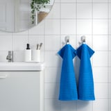 Bright blue VÅGSJÖN towels hang on hooks beside white sink & mirror. Small & neatly folded.