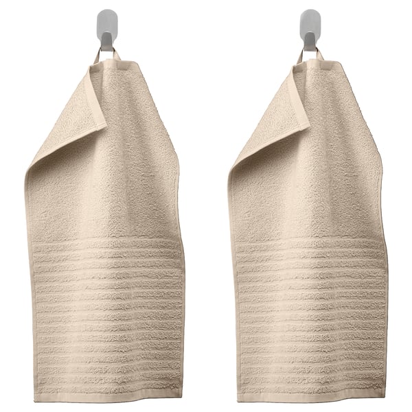 Two beige VÅGSJÖN towels hang side-by-side, featuring textured stripes and solid terry sections, suspended from silver hooks.