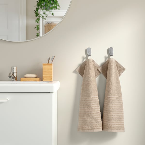Beige VÅGSJÖN towels hang on hooks beside a white vanity, mirror, and toothbrush holder.